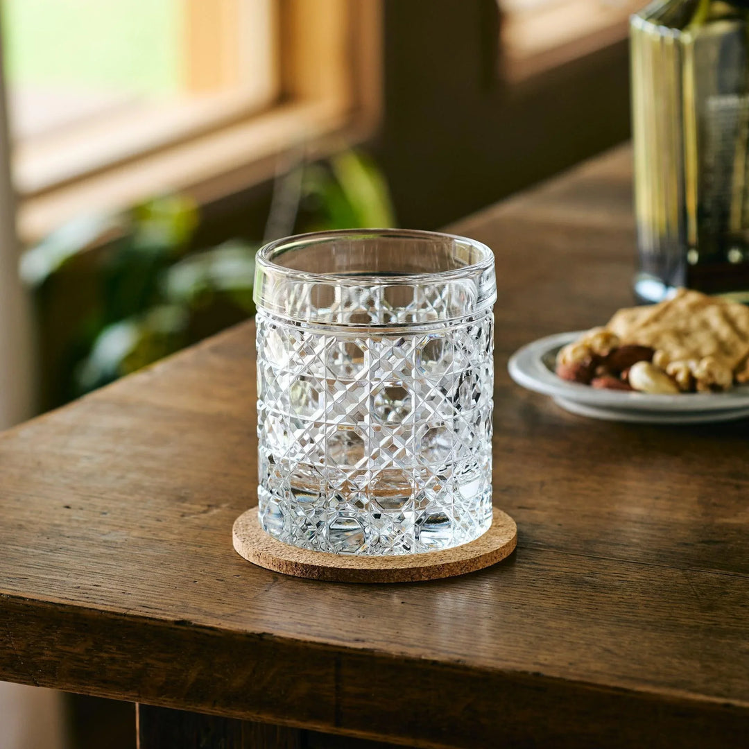 Empty cut Japanese whiskey glass with a lattice pattern, placed on a cork coaster on a wooden table.