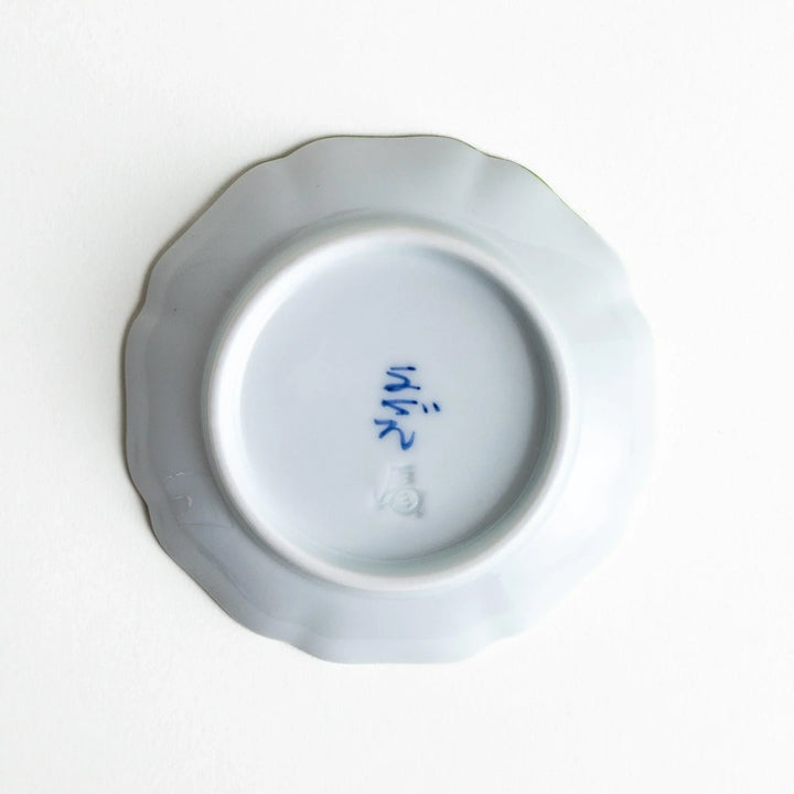 A white ceramic plate with a scalloped edge, featuring a delicate vine pattern in green and red around the border.