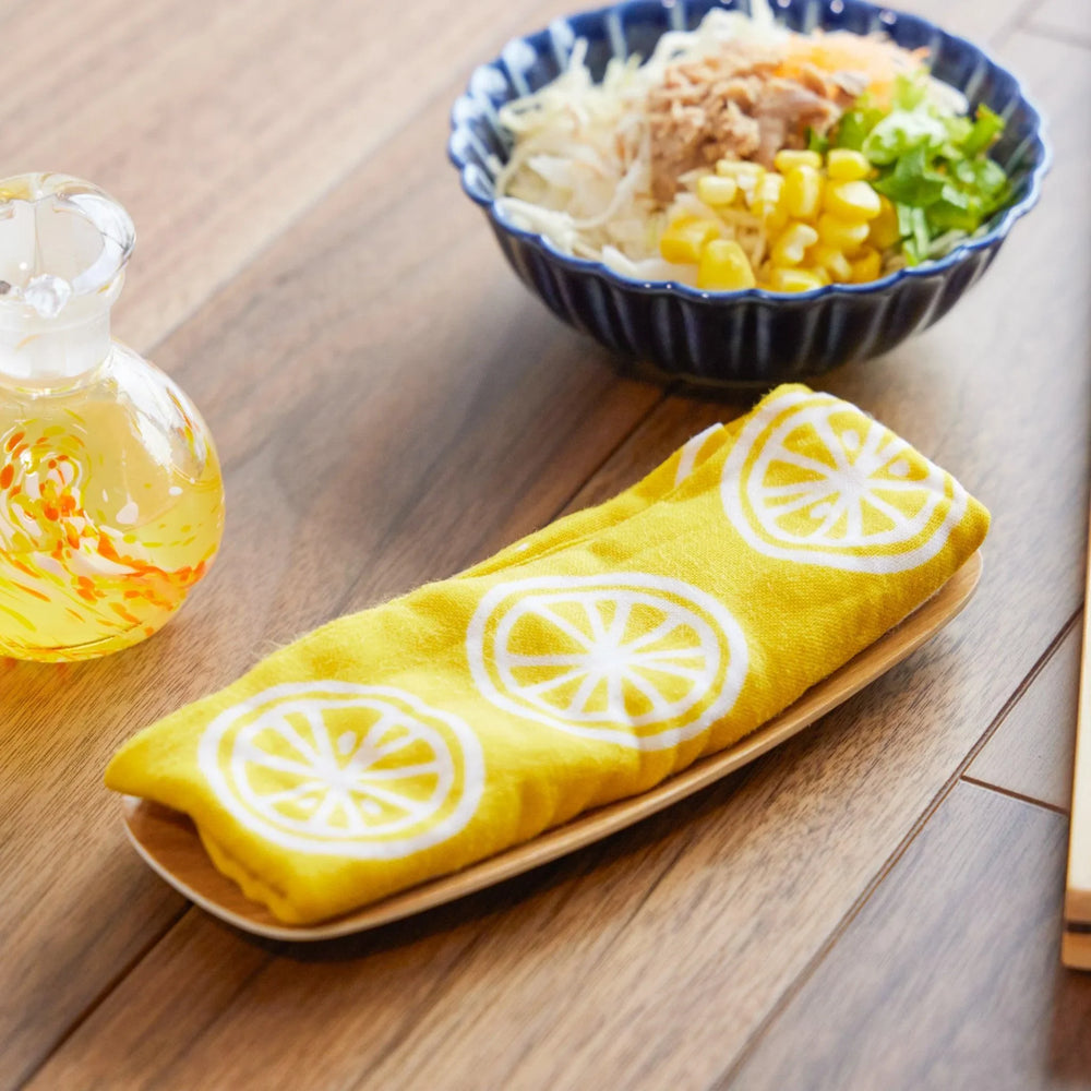 Yellow Japanese tenugui cloth with white lemon slice patterns, neatly folded on a wooden tray.