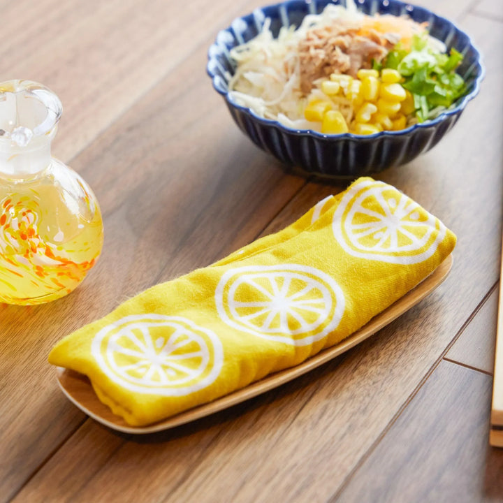 Yellow Japanese tenugui cloth with white lemon slice patterns, neatly folded on a wooden tray.