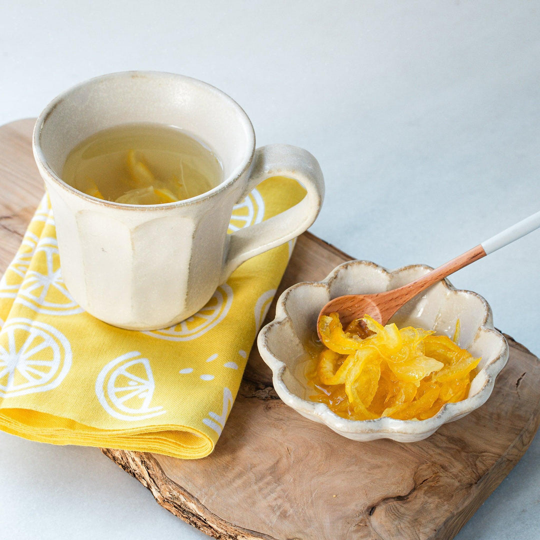 Rustic mug with yuzu tea and syrup in small bowl wooden spoon and lemon napkin for bright table.