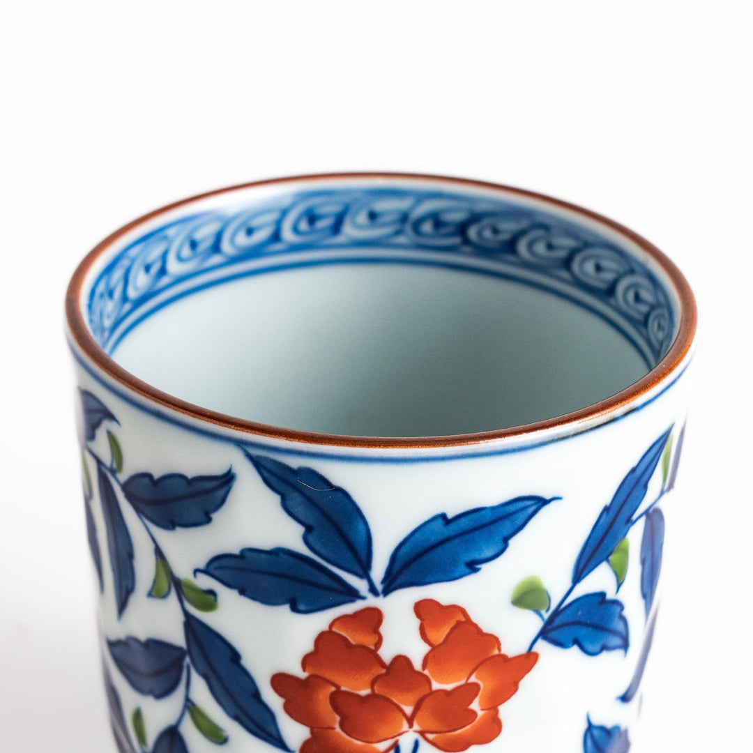 Porcelain teacup with vivid blue and orange floral design and green leaves showing fine Japanese artistry.