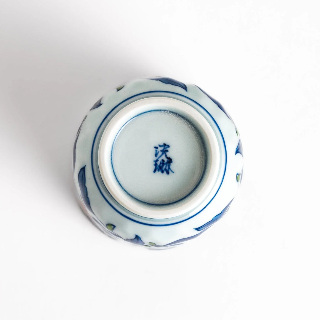 Porcelain teacup with vivid blue and orange floral design and green leaves showing fine Japanese artistry.