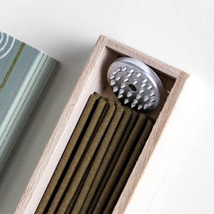 Green incense sticks in a light wooden box with soft green packaging featuring white circular patterns design.