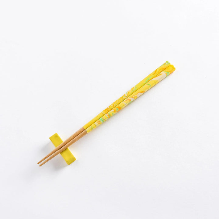 Marbled yellow, green, and orange chopsticks resting on a matching yellow chopstick rest, displaying a fusion of colors.