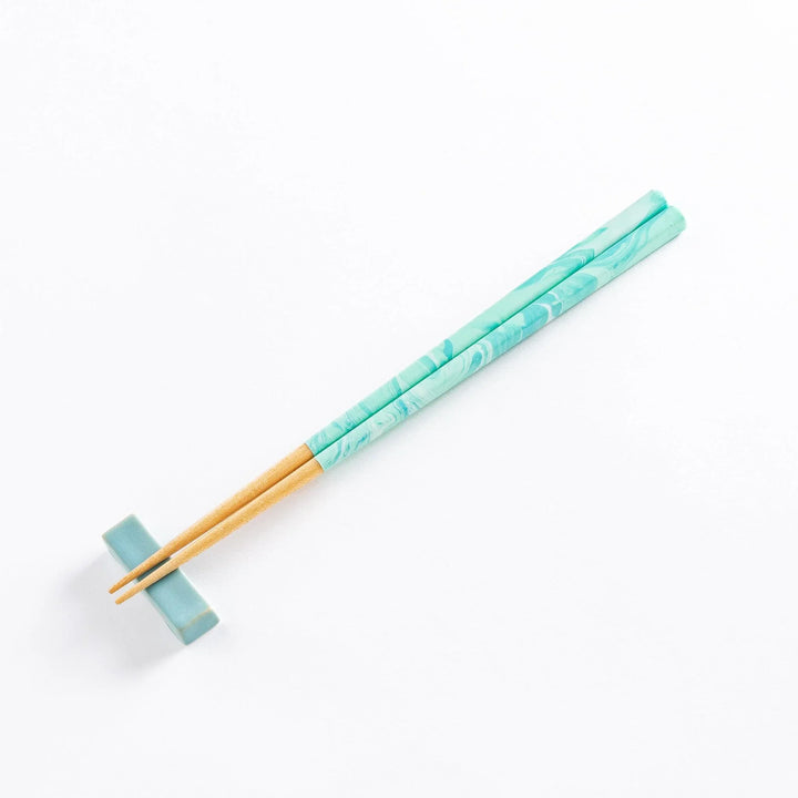 Aqua chopsticks resting in a beautiful curved chopstick rest, showcasing their design and style.