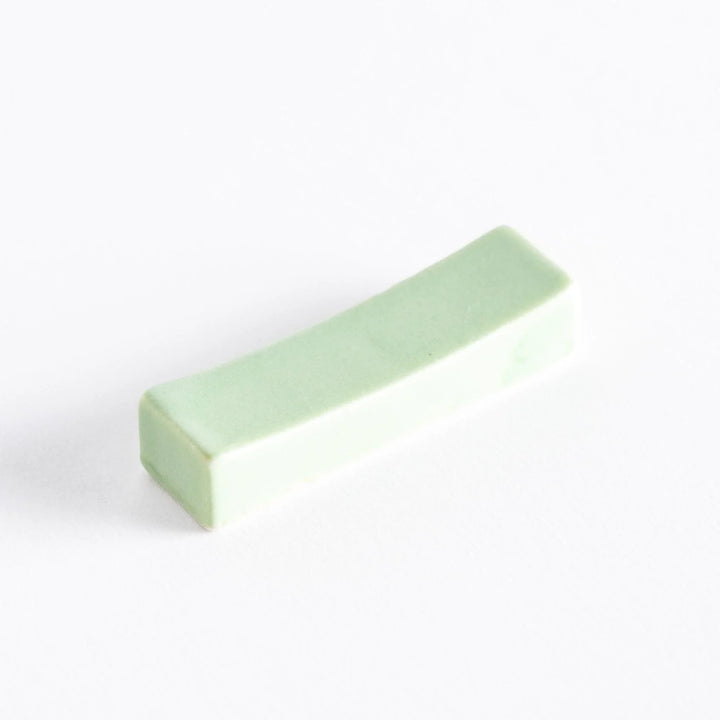A soft green ceramic chopstick rest, with a smooth and curved surface, adding a delicate touch to your dining table.