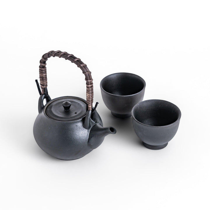 Matte black Japanese ceramic teapot with rattan handle and two matching teacups for elegant tea serving.