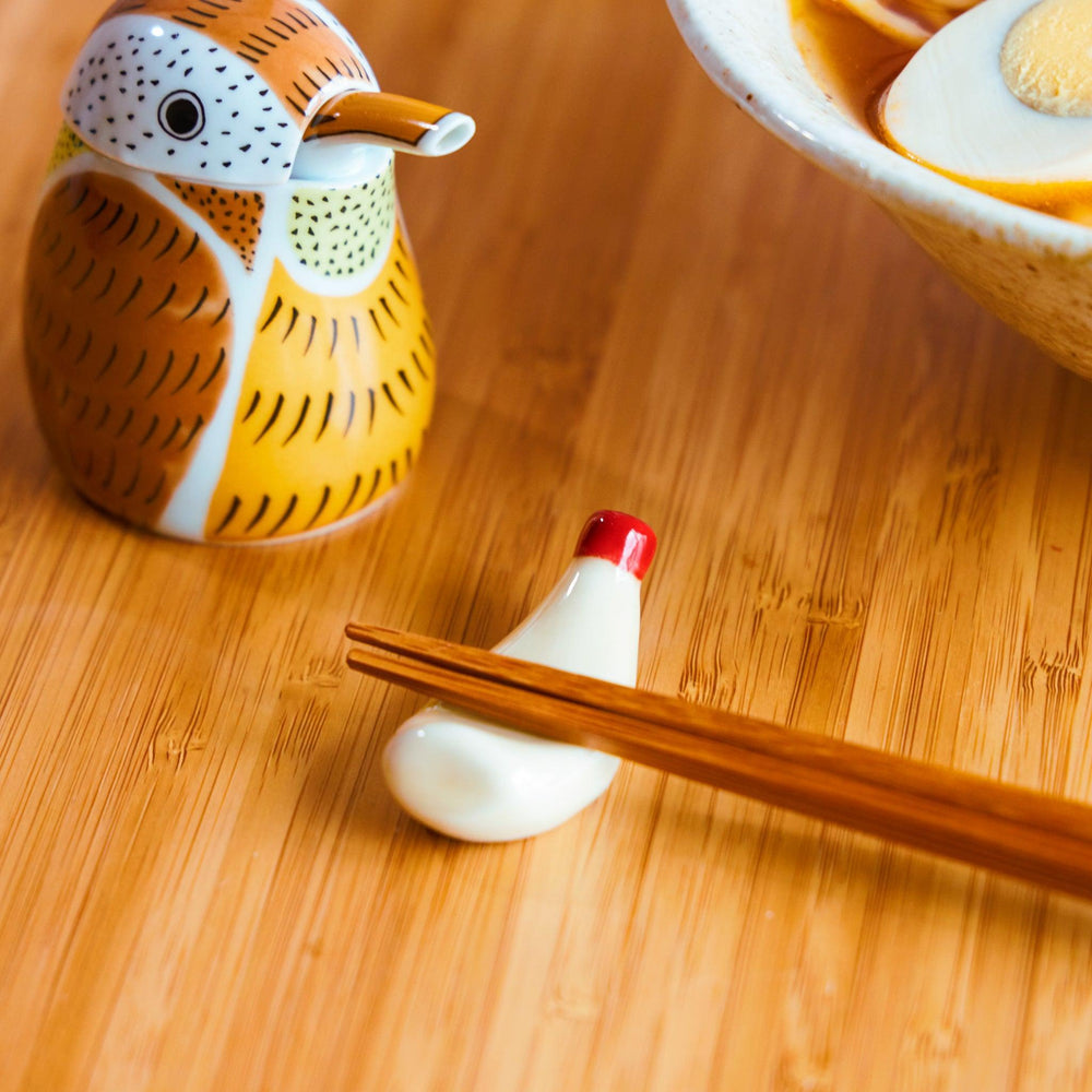 Mayonnaise bottle-shaped chopstick rest with wooden chopsticks, alongside a Red Sparrow soy sauce dispenser and ramen bowl.