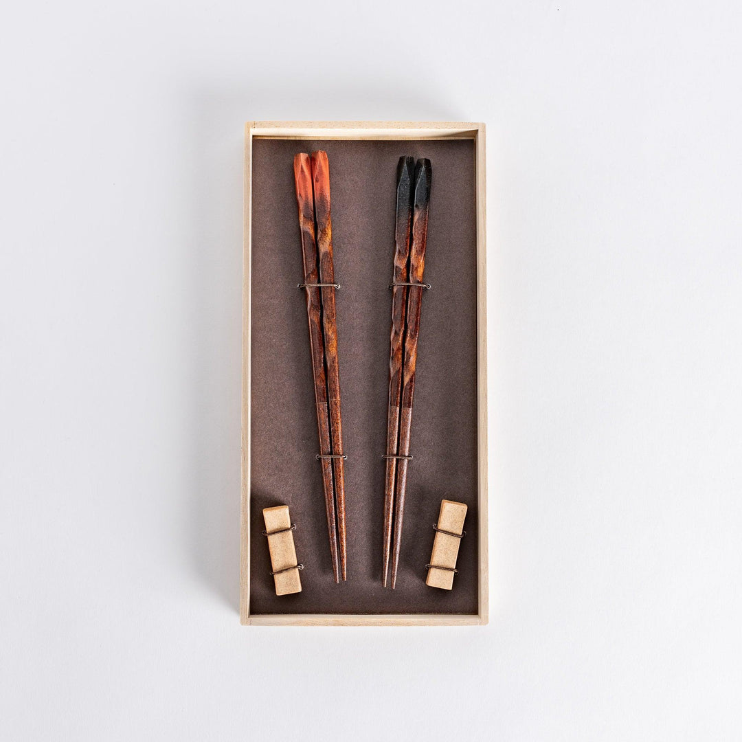 Dark brown chopsticks with textured design and matching rests neatly arranged in wooden presentation box.