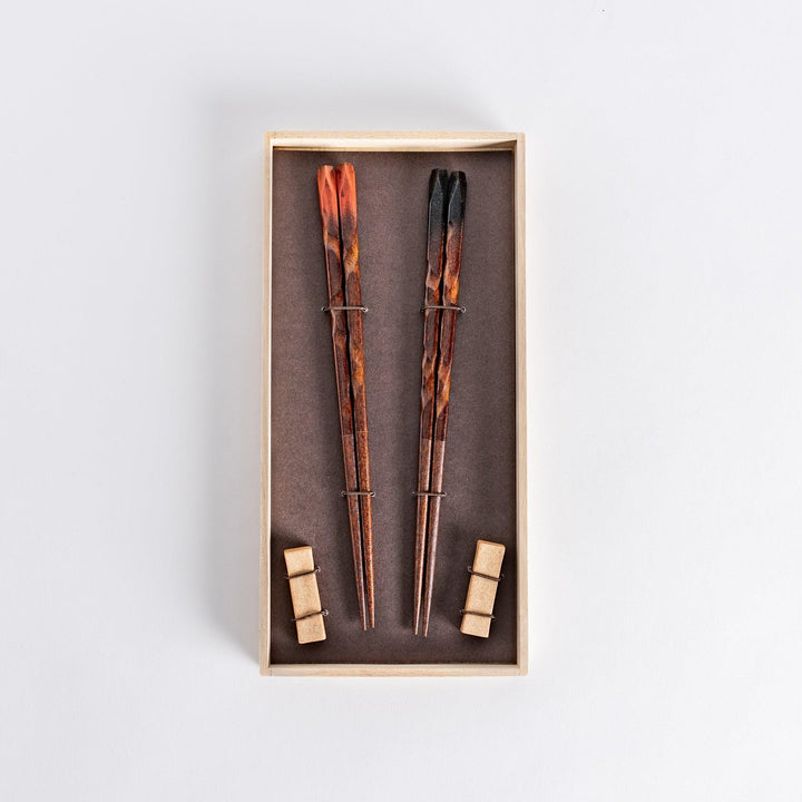 Dark brown chopsticks with textured design and matching rests neatly arranged in wooden presentation box.