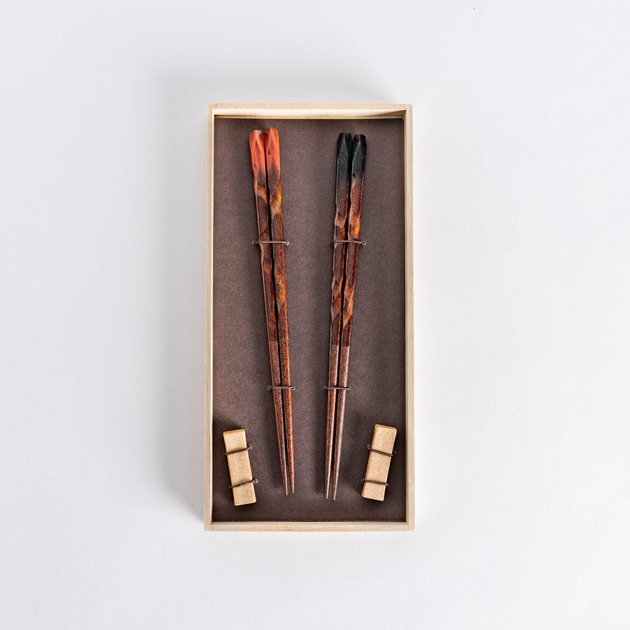 Dark brown chopsticks with textured design and matching rests neatly arranged in wooden presentation box.