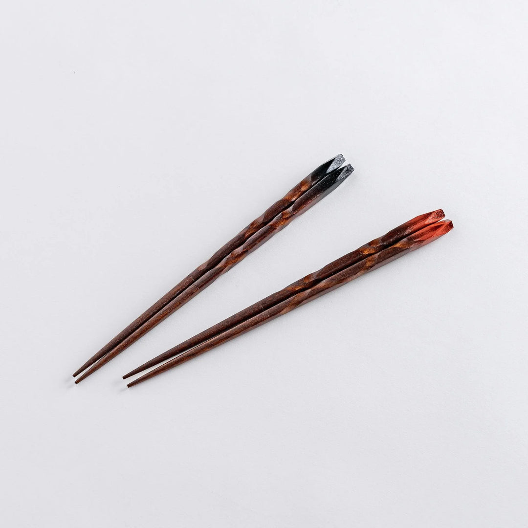 Chopsticks with blackened tips, delicately crafted with a spiral pattern and a beige chopstick rest placed underneath.