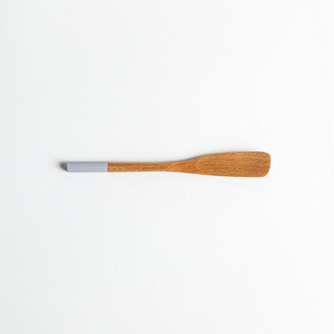 A set of four wooden spatulas with flat tips, each featuring a different colored end—white, black, blue, and red