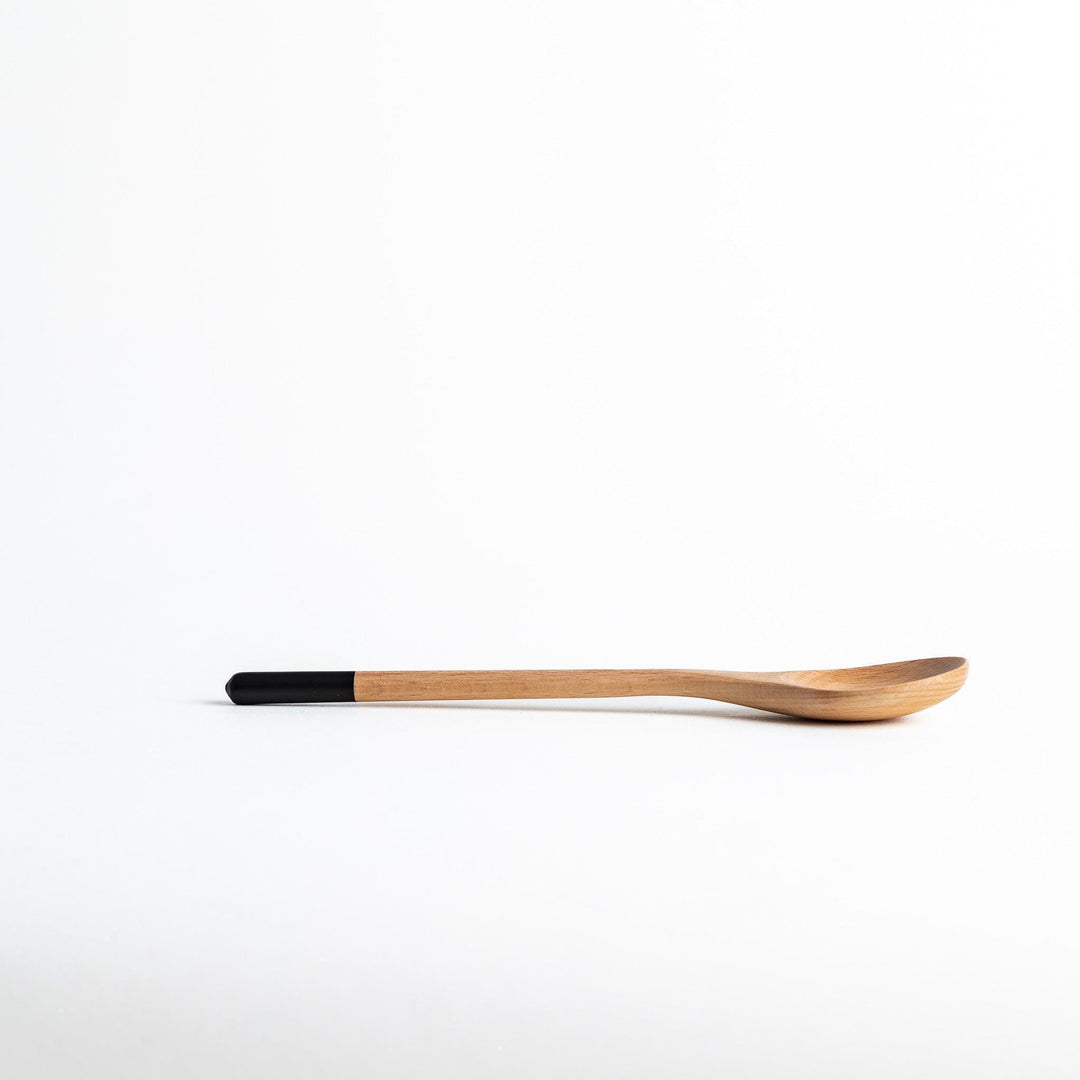 A set of four wooden soup spoons with wide, rounded bowls and colored tips—white, black, blue, and red.