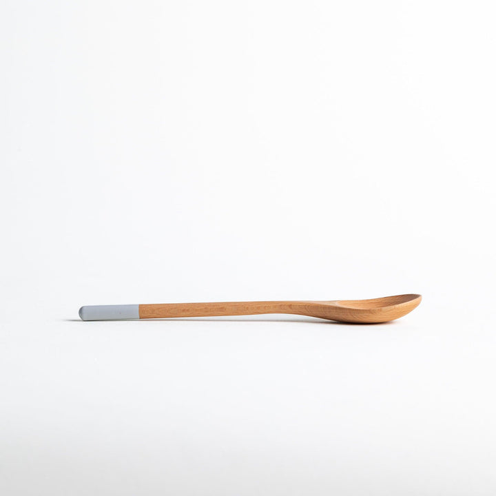 A set of four wooden soup spoons with wide, rounded bowls and colored tips—white, black, blue, and red.