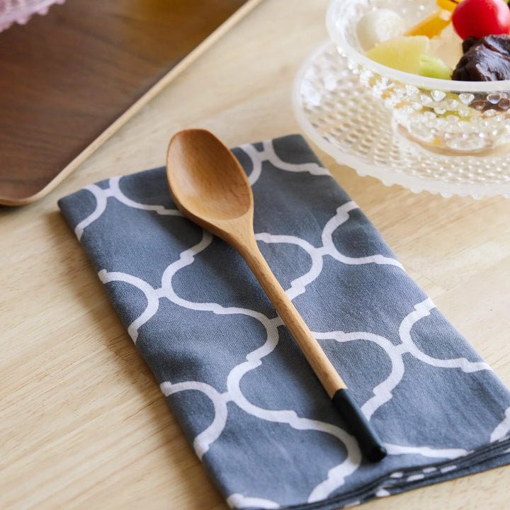 Natural wood spoon with a smooth curved bowl and matte black dipped handle, placed on a soft cotton tenugui cloth.