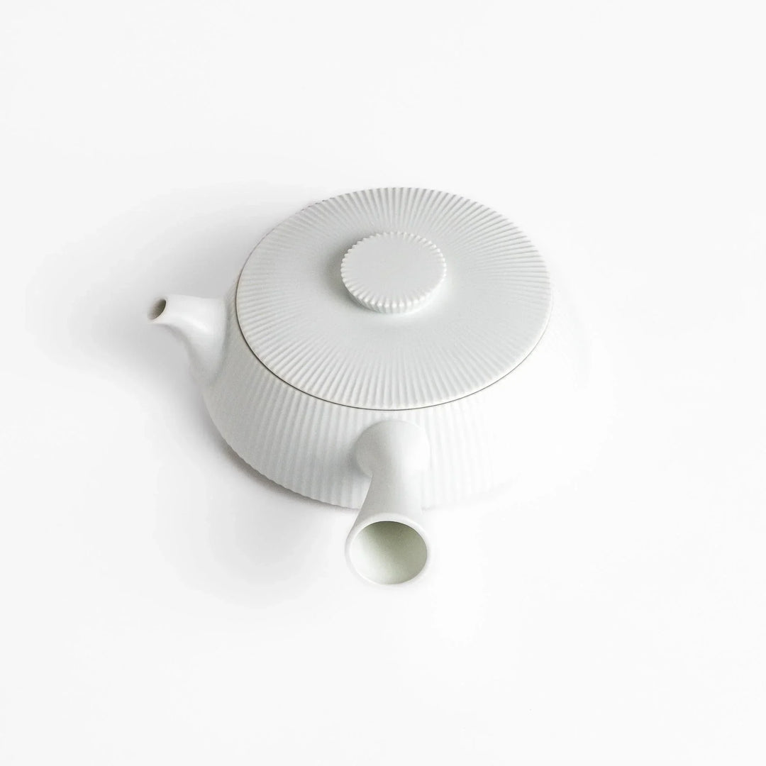 Minimalist ribbed white teapot with sleek spout and round textured lid adding elegance to modern tea sets.