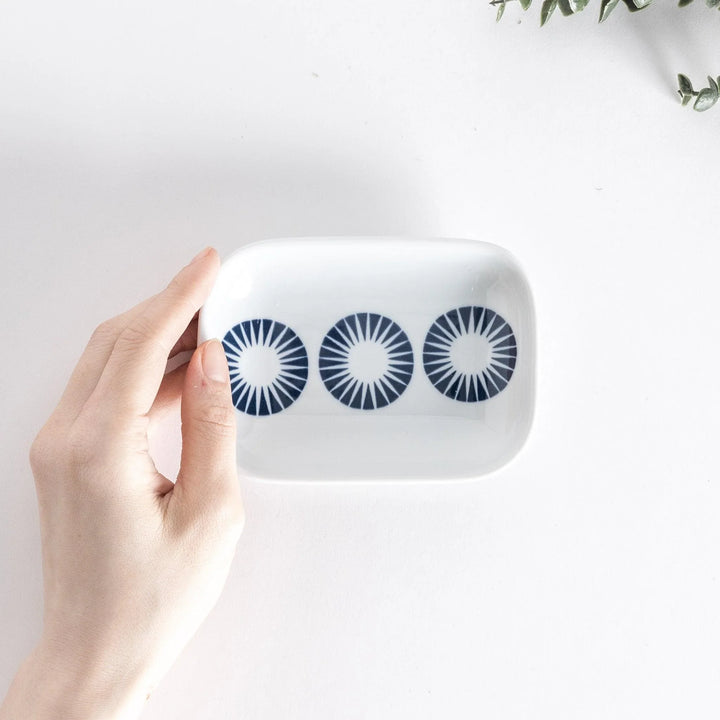 Top view of the sauce dish held in hand, showing three navy blue circles with radiating lines on a white surface.