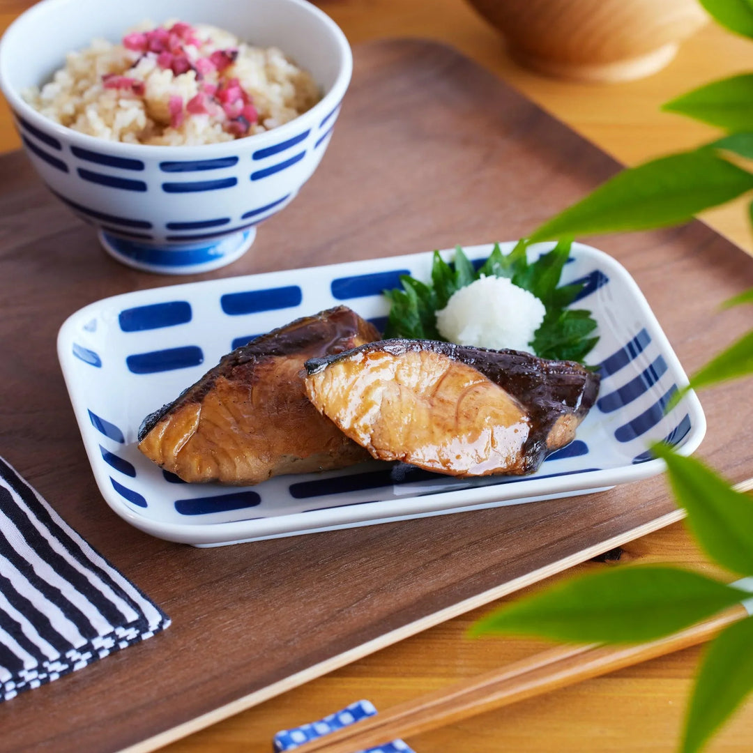 A rectangular dessert plate with modern indigo brushstroke patterns, beautifully presenting grilled fish and grated daikon.