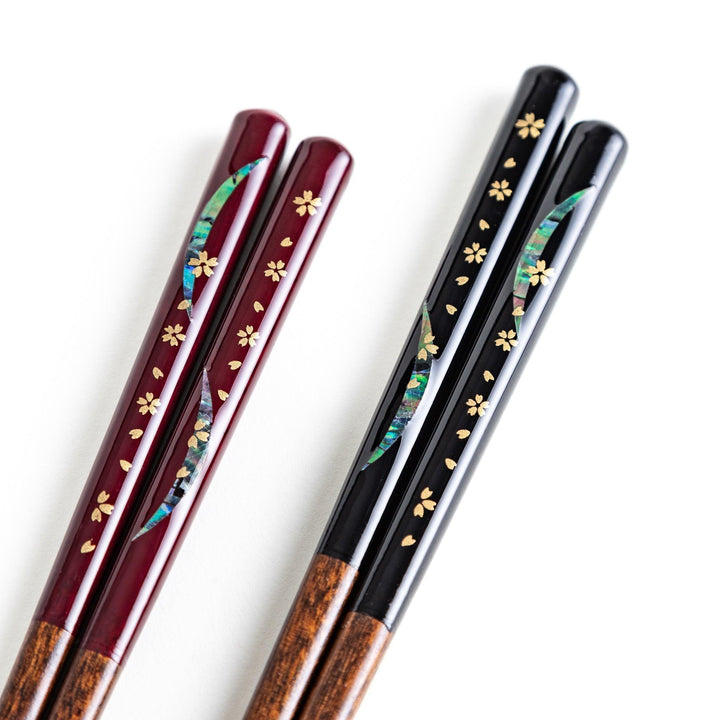 Two pairs of chopsticks, one with red and one with black handles, featuring moon and sakura design.