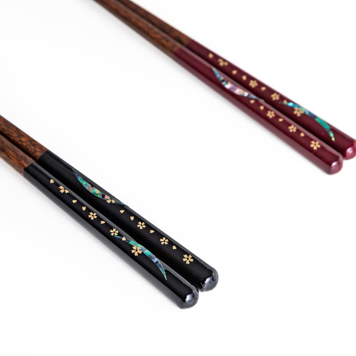 Two pairs of chopsticks, one with red and one with black handles, featuring moon and sakura design.