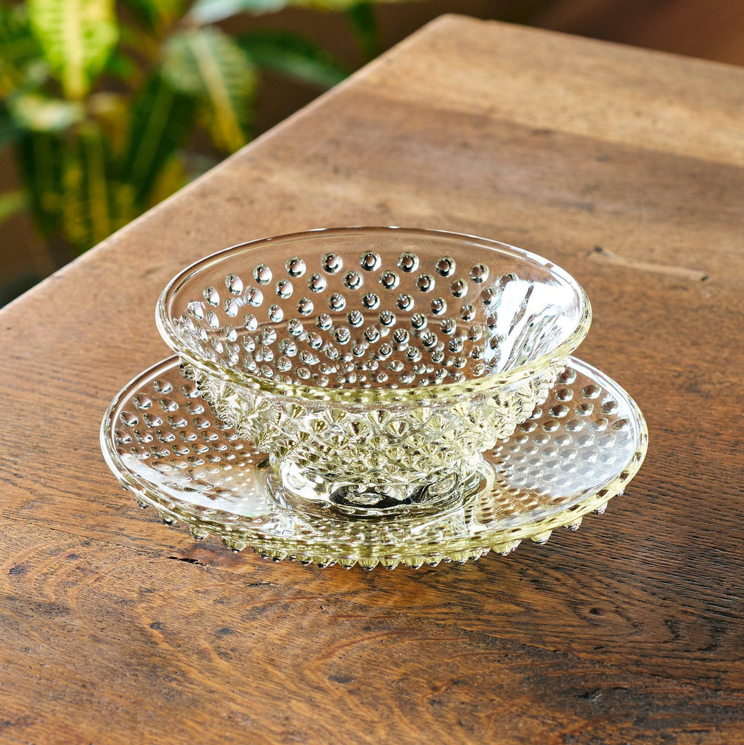 Amber glass dessert bowl and saucer with raised dots and starburst base, perfect for serving refined sweets.