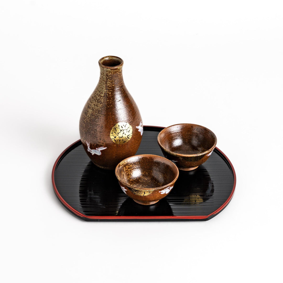 Brown ceramic sake set with rabbit and moon design including carafe and cups on tray for sharing.