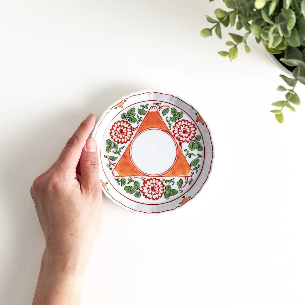 Hand holding porcelain plate with floral and geometric pattern viewed from above showing interior design.