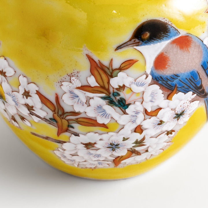 Yellow vase with cherry blossoms and colorful bird design bringing a bright touch of spring to decor.