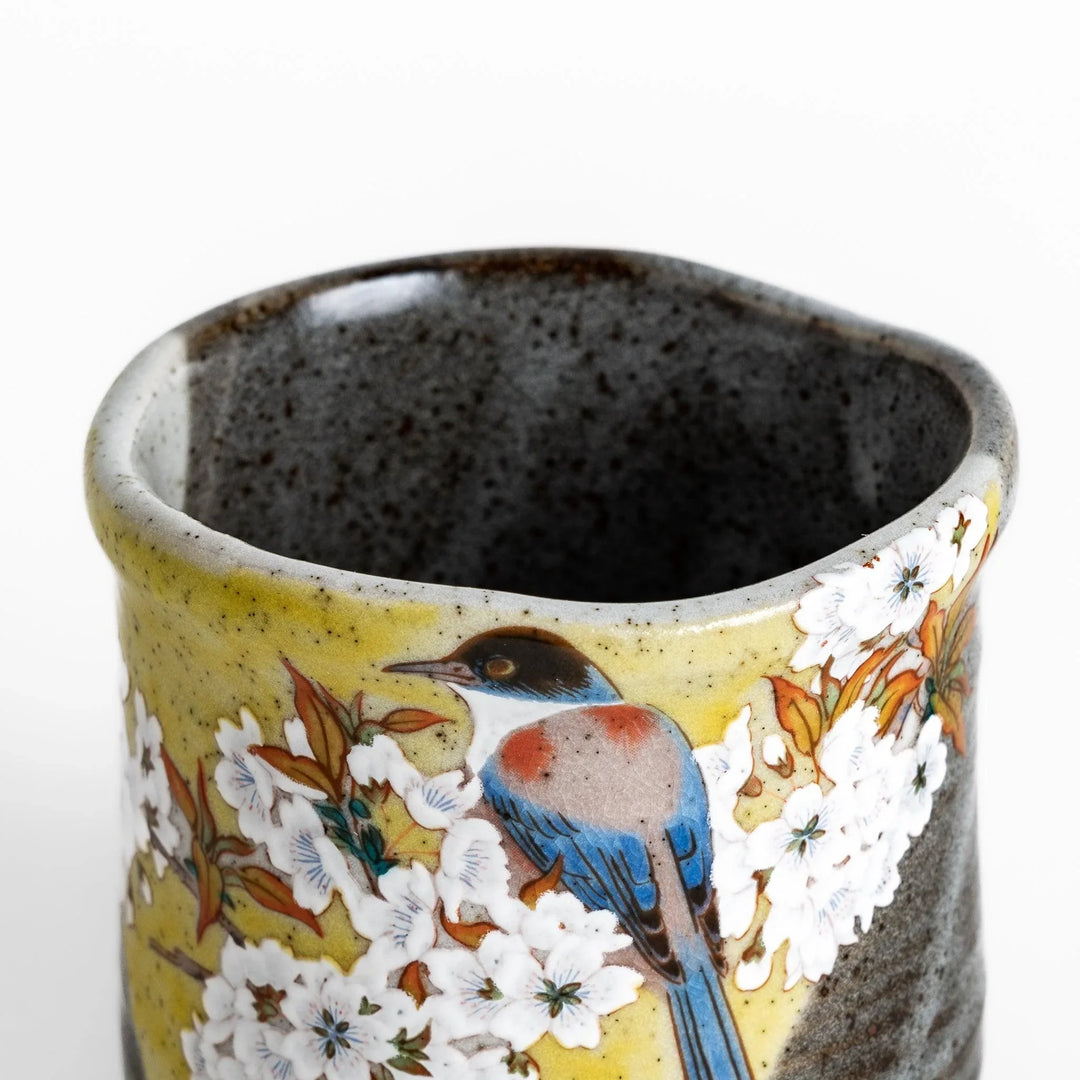 Tea Cup featuring a bird perched on blooming sakura flowers, set against a yellow and gray background.