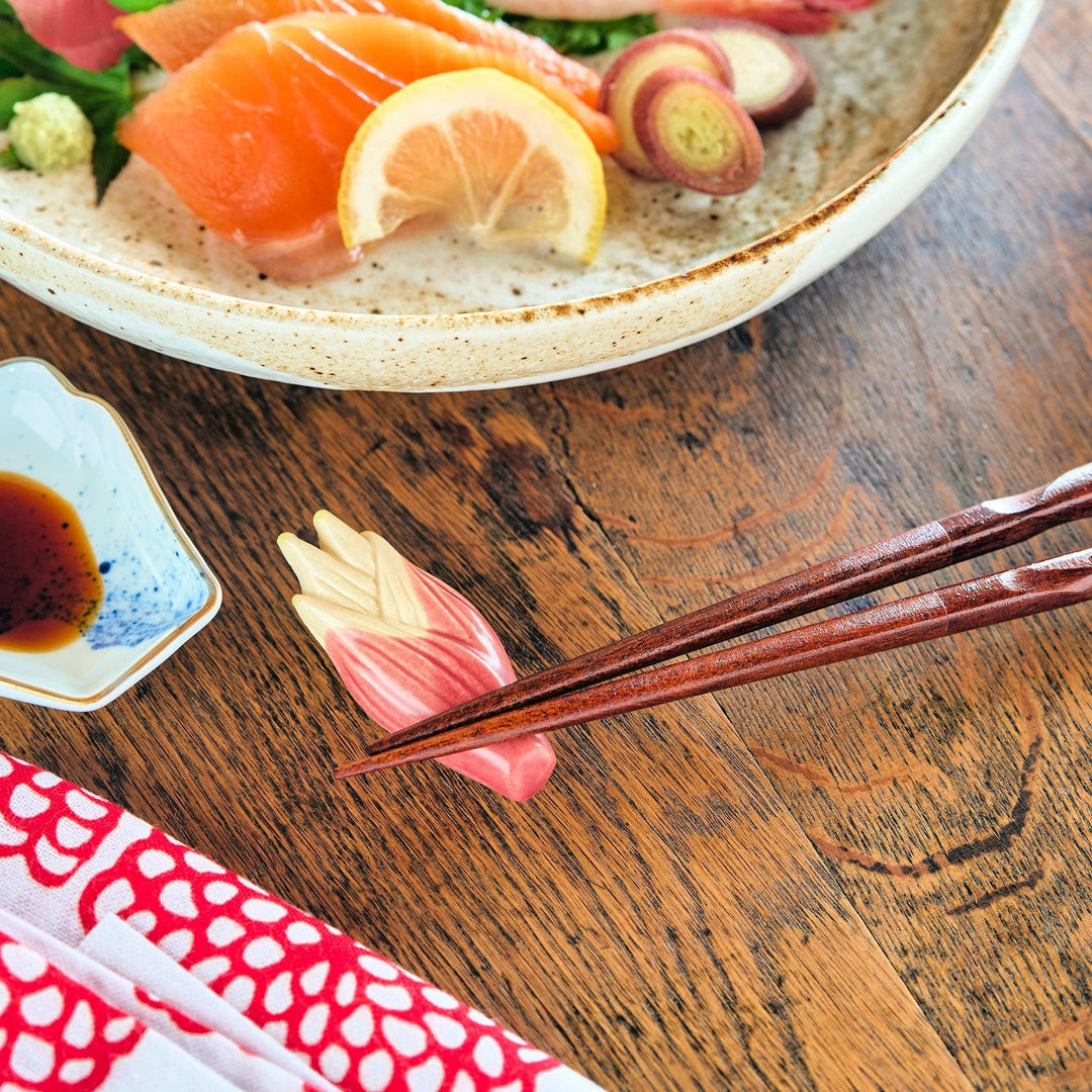 Myoga ginger ceramic chopstick rest in pink and cream tones placed beside sashimi and blue sauce dish.