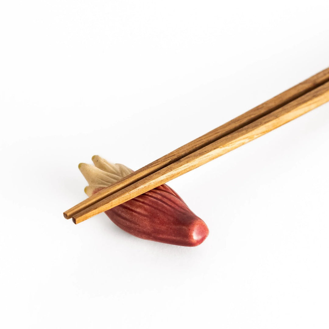 Myoga ginger ceramic chopstick rest in pink and cream tones placed beside sashimi and blue sauce dish.