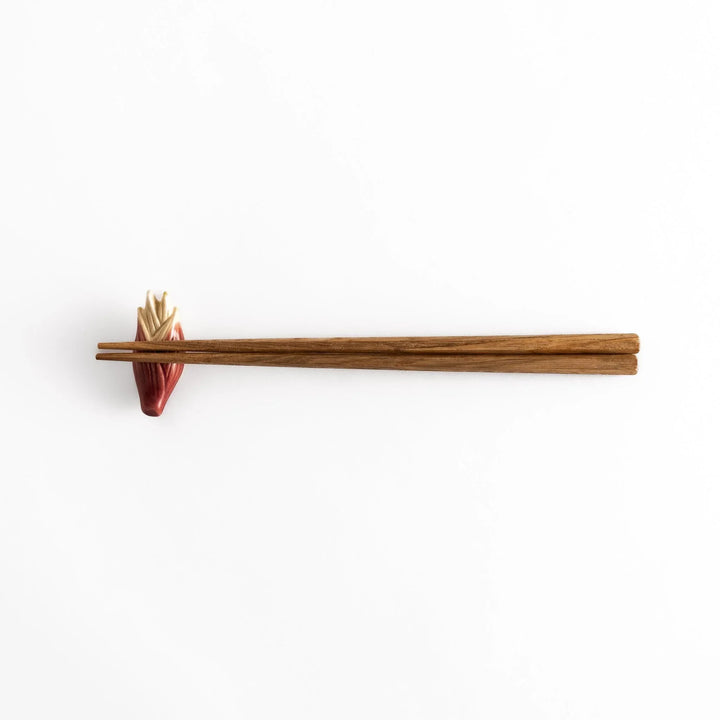 Myoga ginger ceramic chopstick rest in pink and cream tones placed beside sashimi and blue sauce dish.