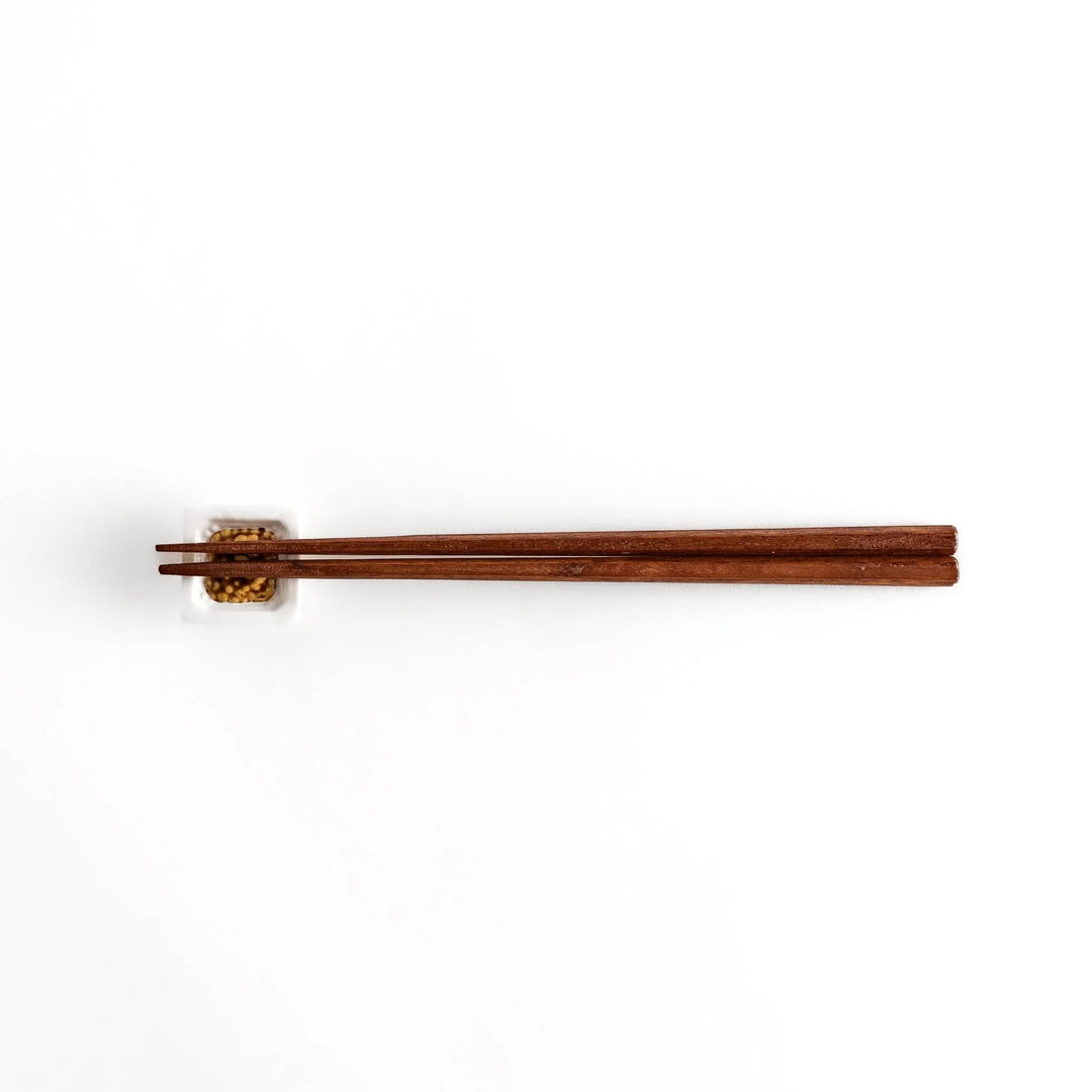 A pair of chopsticks resting on the natto-inspired square chopstick rest, displayed from a distance for an overall view.