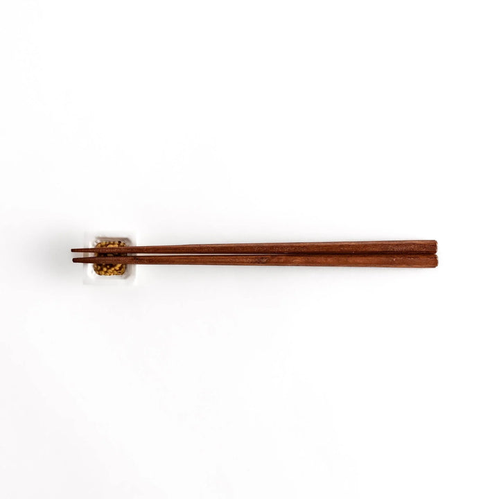 A pair of chopsticks resting on the natto-inspired square chopstick rest, displayed from a distance for an overall view.