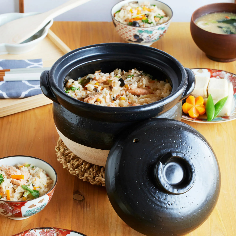 Japanese black and white donabe clay pot filled with freshly cooked takikomi gohan, surrounded by miso soup and side dishes.