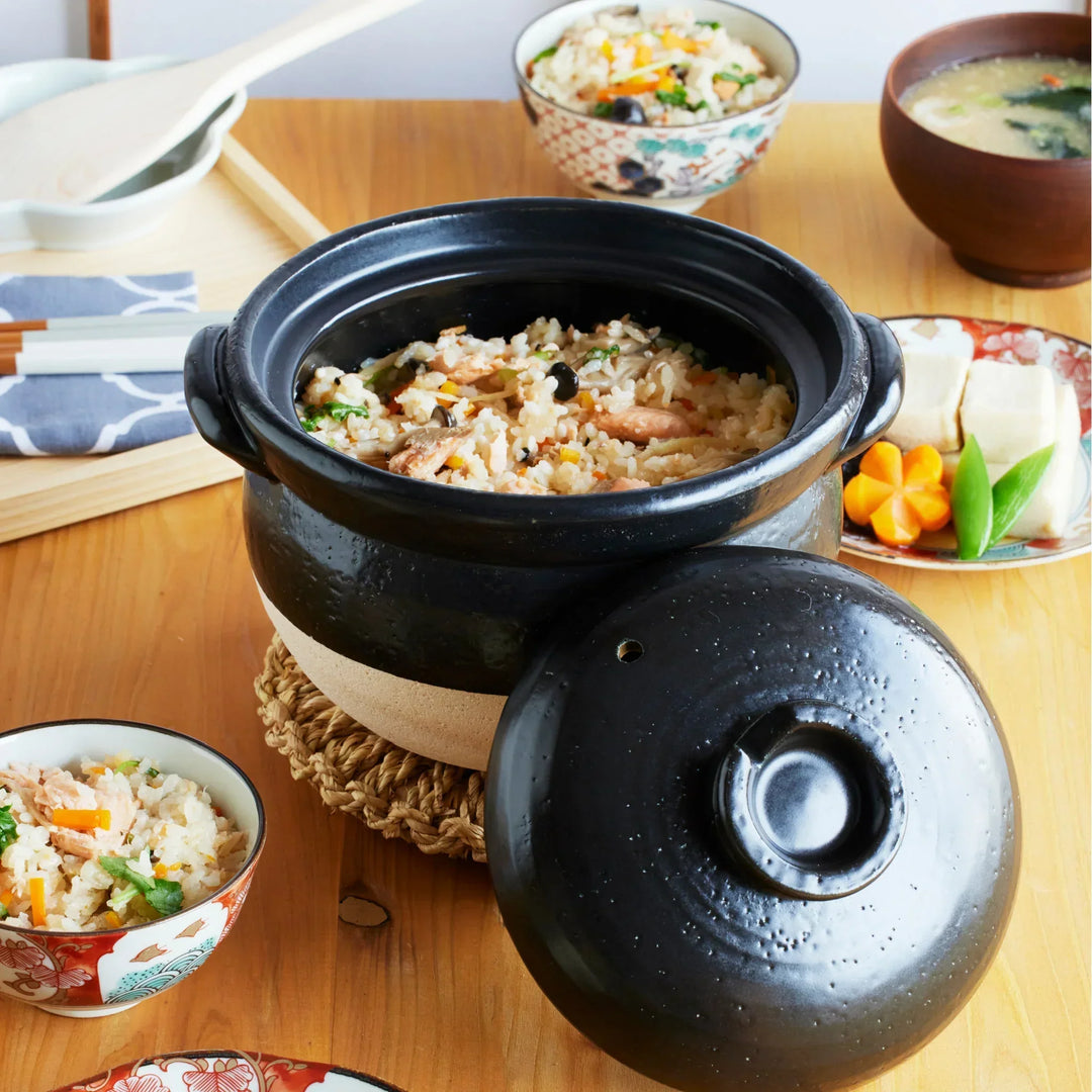 Japanese black and white donabe clay pot filled with freshly cooked takikomi gohan, surrounded by miso soup and side dishes.