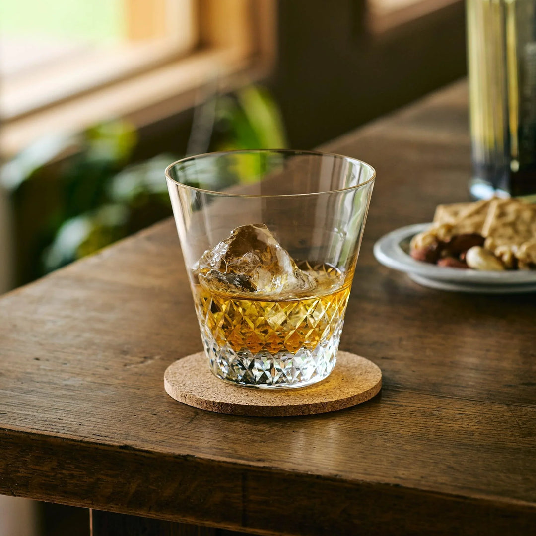 Diamond-cut Japanese whiskey glass filled with whisky and a large ice cube, set on a cork coaster.