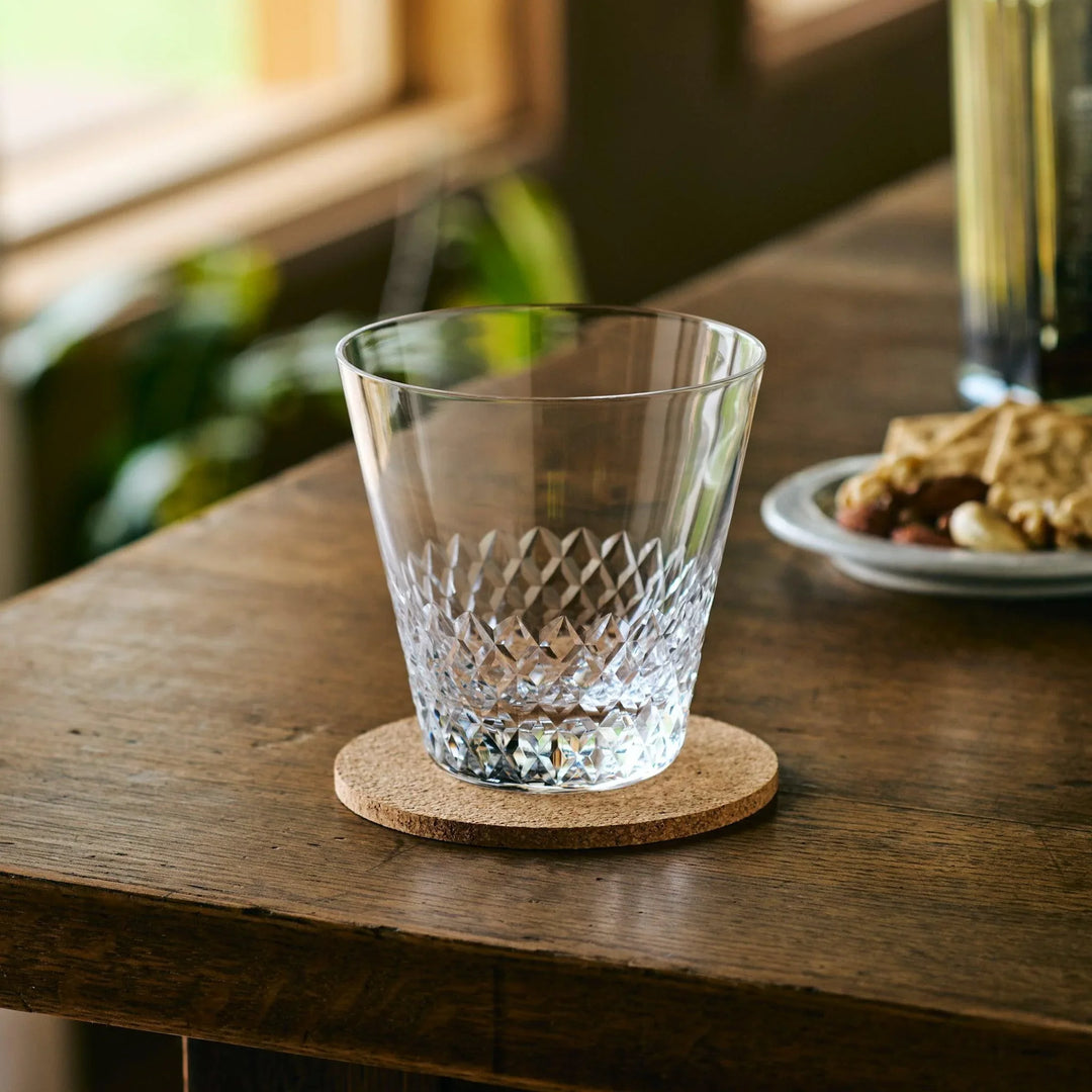 Empty Japanese whiskey glass with diamond-cut pattern, placed on a cork coaster on a wooden table.