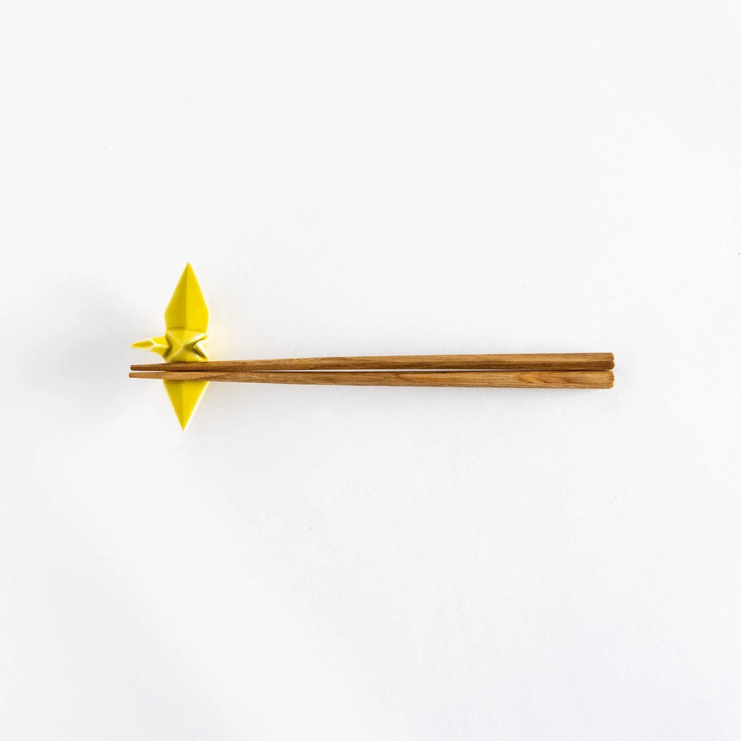 Wide view of chopsticks resting on the yellow ceramic crane-shaped chopstick rest.