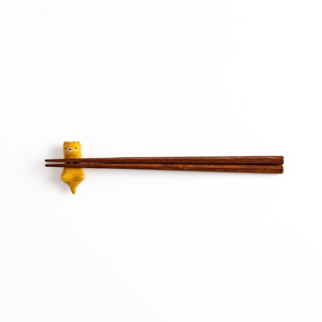 Otter Chopstick Rest holding wooden chopsticks, showcasing its playful and functional design with a glossy yellow finish.