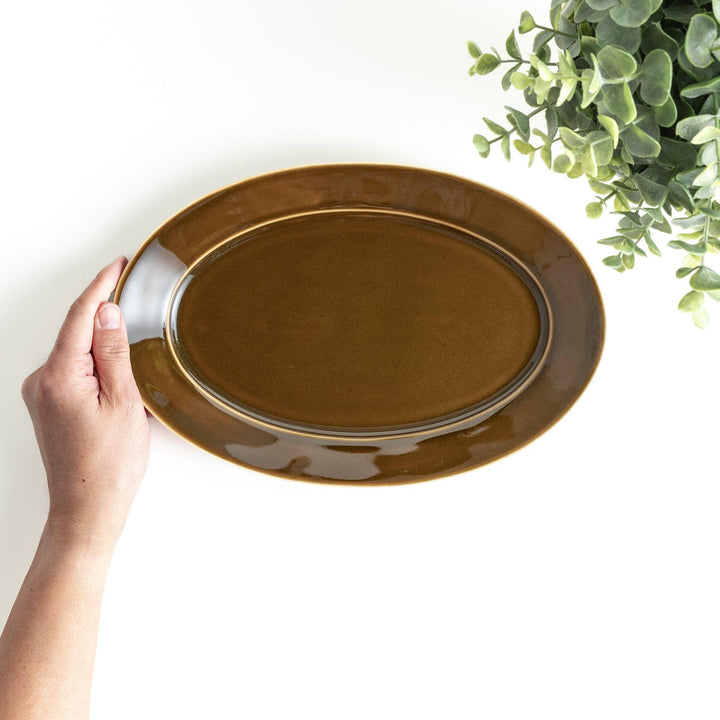 Sleek, dark brown or olive colored oval dinner plate with a glossy finish, simple and minimalist.