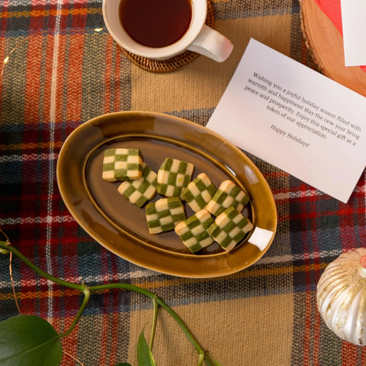 Oval salad plate with green and yellow patterned food cup of tea and festive note on wooden table.