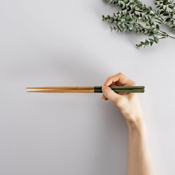 Hand holding green-tipped cooking chopsticks with bamboo shafts, showcasing a sleek and functional design.