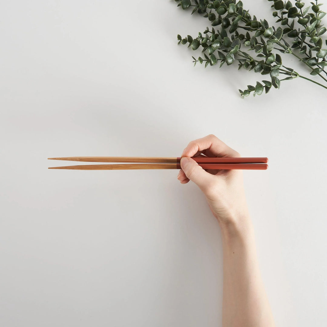 A hand holding the red-tipped chopsticks, demonstrating their comfortable grip and usage.