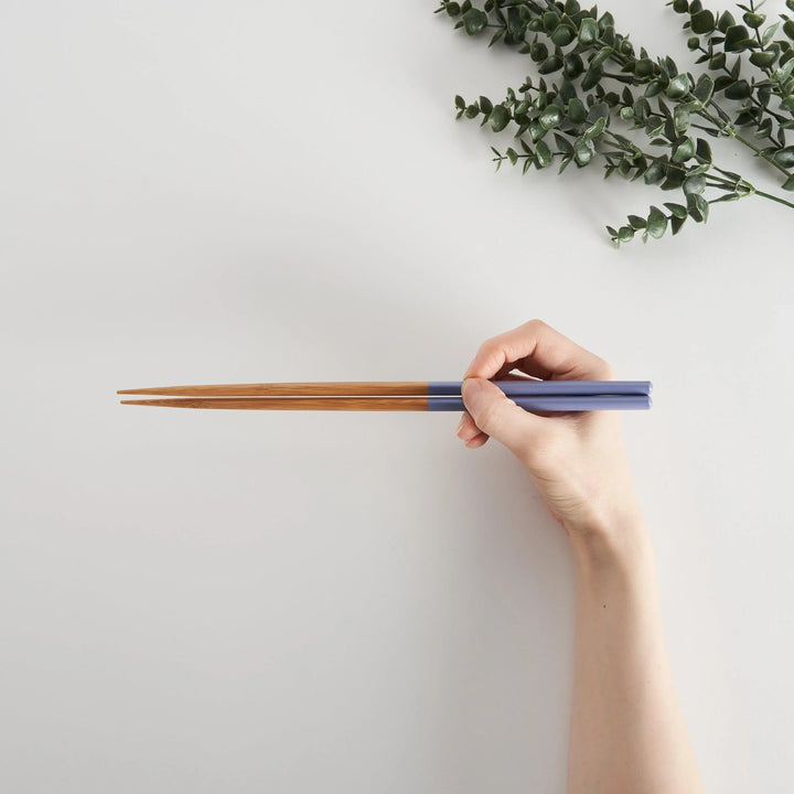 Bamboo cooking chopsticks with soft blue tips held in hand, perfect for cooking.