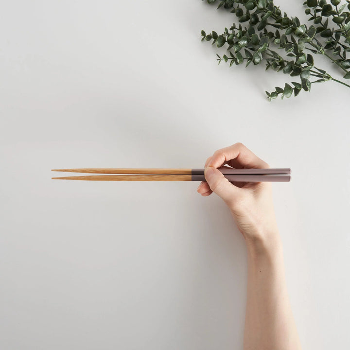 A hand holding cooking chopsticks with pastel rosybrown tips, ideal for precise cooking and serving.