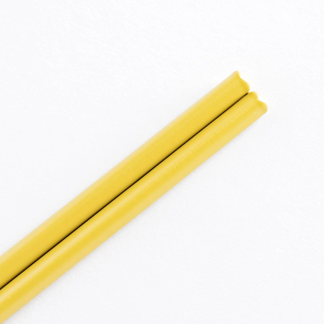 Close-up view of the yellow-painted handles of cooking chopsticks, showing smooth, rounded edges.