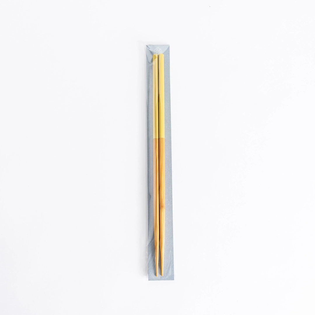 Yellow-tipped cooking chopsticks in sealed packaging, wooden stems visible, set on a neutral background.